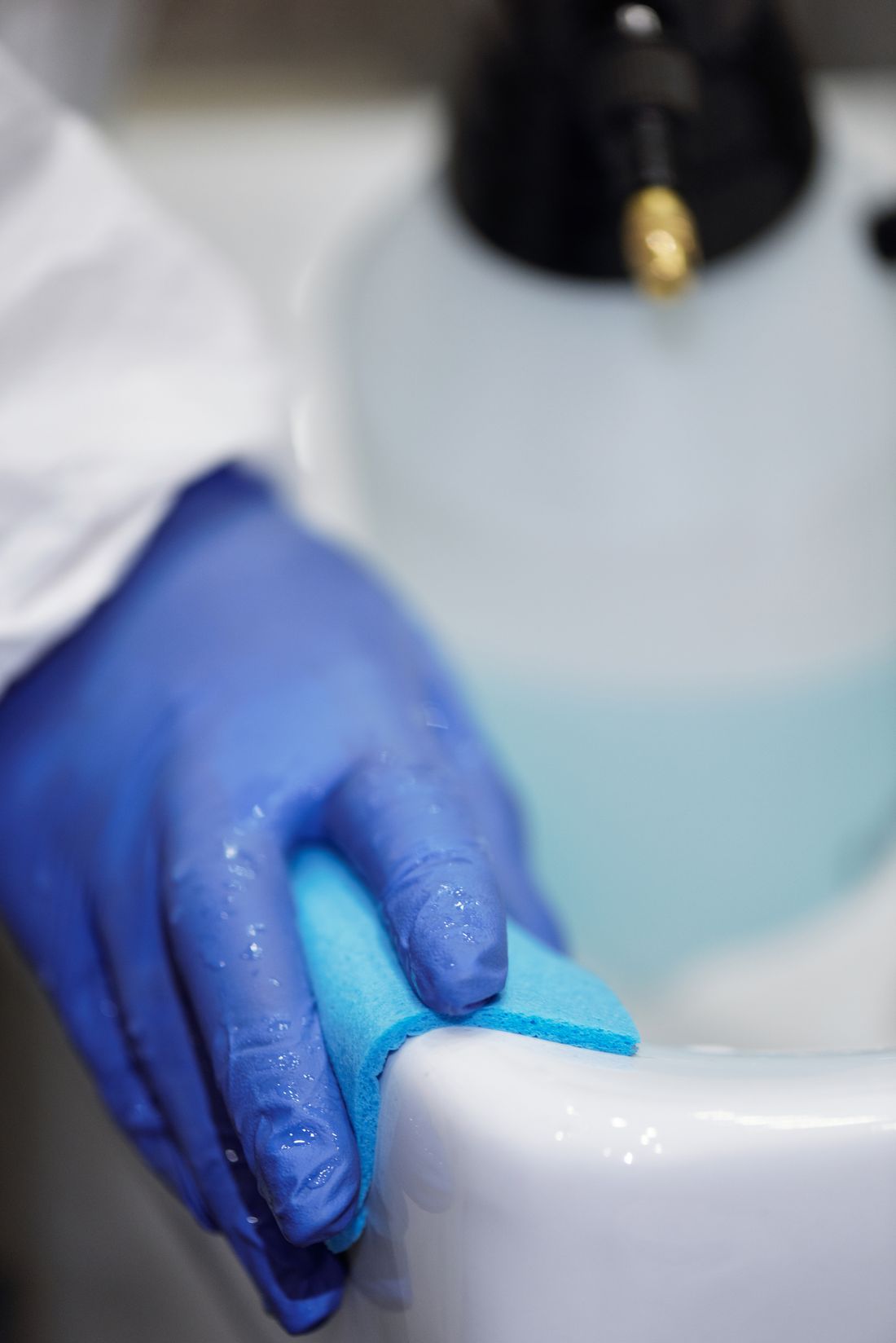 Mà amb guant blau netejant un lavabo blanc amb una esponja