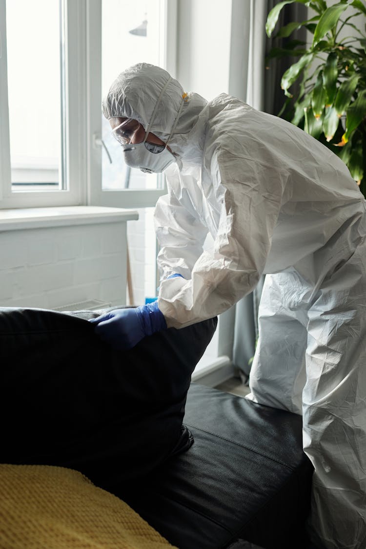 Person Wearing White PPE While Cleaning The Couch