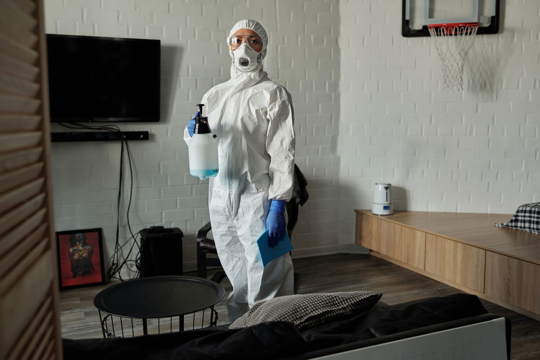 Person in full protective gear disinfecting a living room during health crisis.