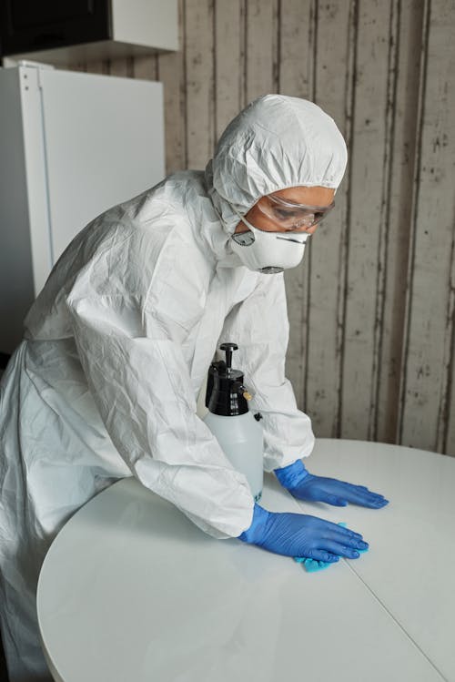 Person in White PPE Cleaning the Table