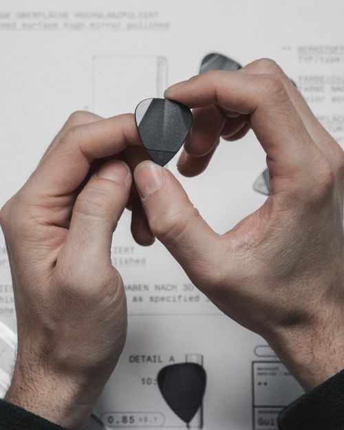 Free Detailed close-up of hands gripping a guitar pick against a technical drawing background. Stock Photo