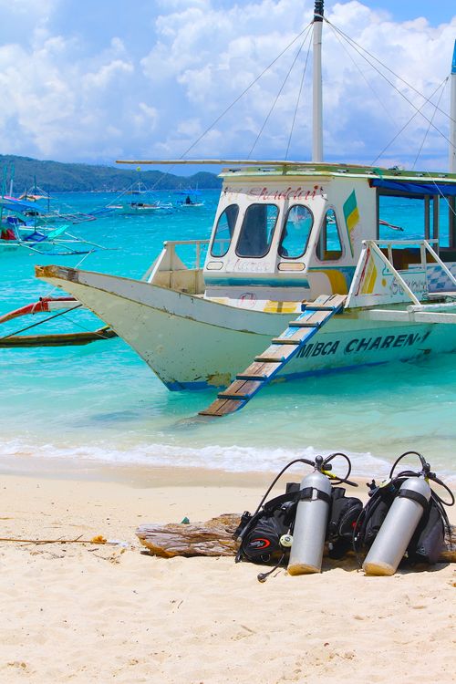 Free Vibrant beach scene in the Philippines featuring dive gear on shore with anchored boats in the turquoise water. Stock Photo