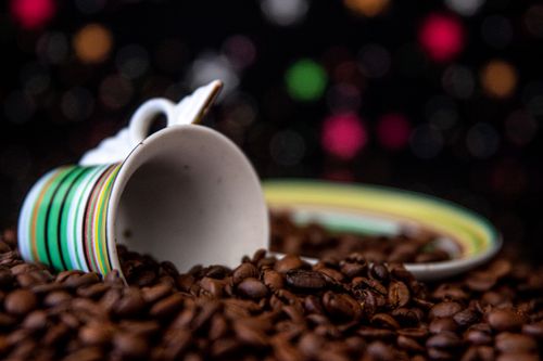 Free An artistic shot of a colorful ceramic mug resting on a bed of coffee beans, creating a vibrant still life scene. Stock Photo