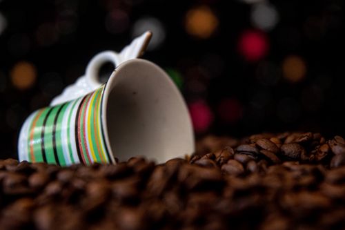 Free Colorful striped mug surrounded by coffee beans with a vibrant bokeh background. Stock Photo