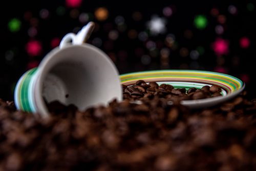 Free Close-up of a tipped striped cup with coffee beans on a dark, bokeh background. Stock Photo