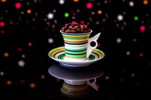 Free A striped cup filled with coffee beans on a reflective black surface with colorful bokeh. Stock Photo