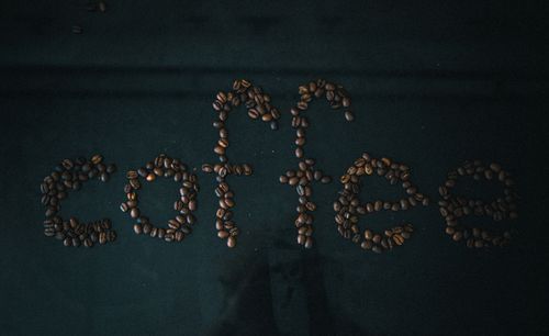 Free Creative arrangement of coffee beans spelling 'coffee' on a dark black surface. Stock Photo
