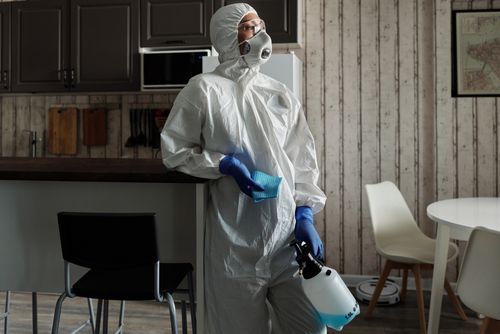 Free Cleaner in PPE suit using a sprayer for disinfection indoors. Focus on safety and hygiene. Stock Photo