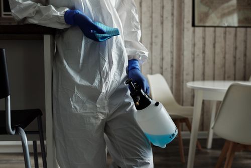 Free Person in protective gear disinfecting with spray in home setting. Stock Photo