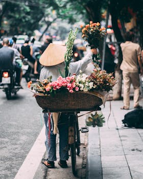 A flower vendor in Hanoi selling colorful bouquets from a bicycle on a bustling street.