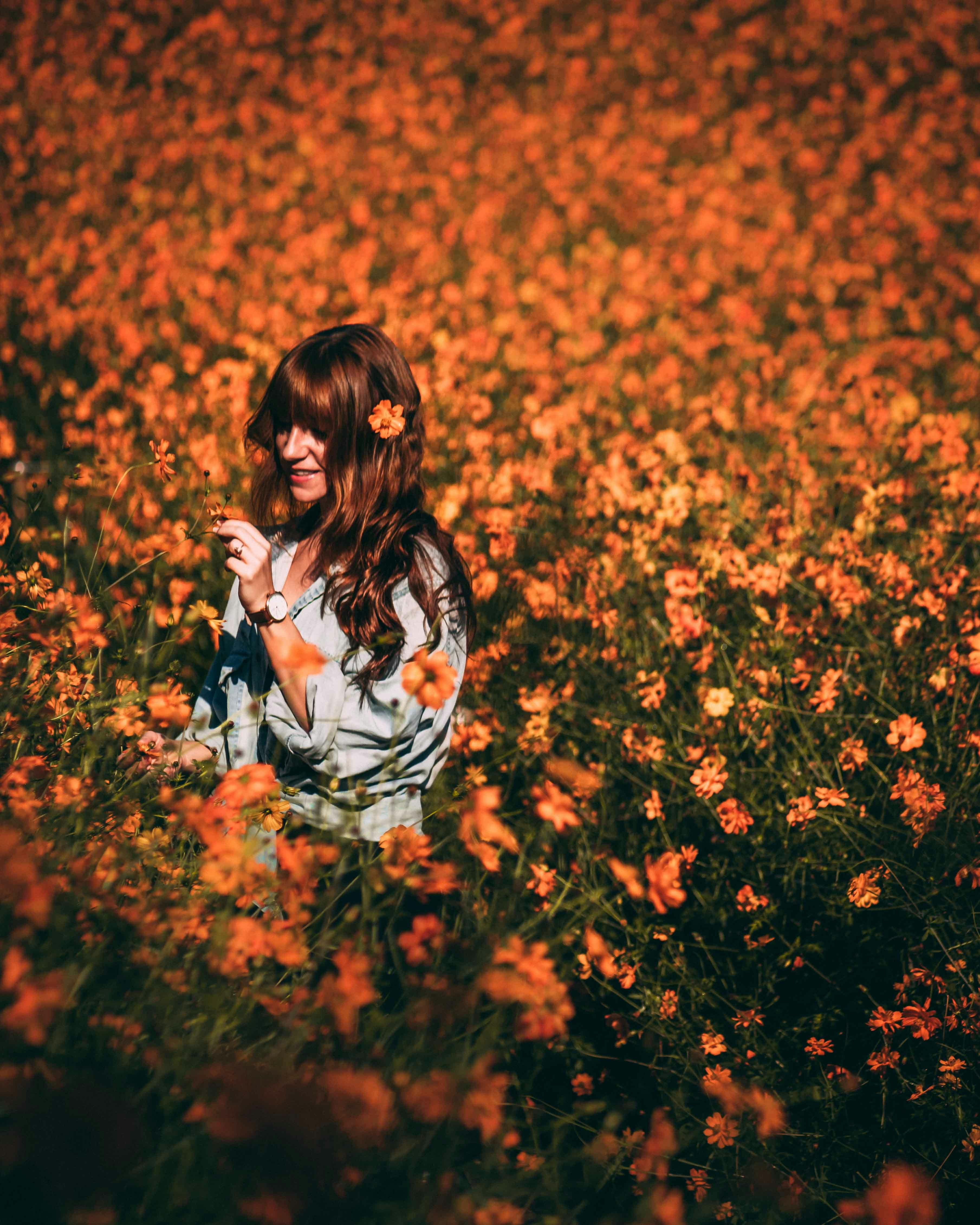 年轻女子在鲜艳的橙色花丛中，享受着阳光明媚的一天