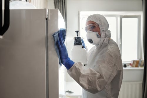 A Woman in White Coveralls Cleaning a Refrigerator