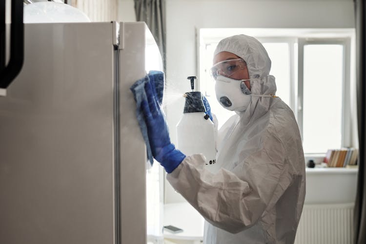 A Woman In White Coveralls Cleaning A Refrigerator