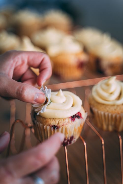 Free Close-up of a hand decorating cupcakes with creamy icing and flowers, capturing the essence of homemade baking. Stock Photo