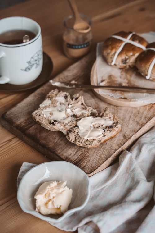Free Warm rustic breakfast spread featuring hot cross buns, butter, and a cozy tea setup. Stock Photo