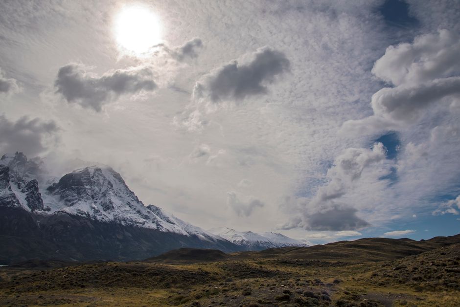 Scenic view of snowcapped Torres del Paine mountains under a bright sun and cloudy sky.