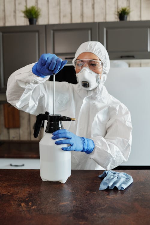 Free Person in White Protective Suit Holding Black and Blue Plastic Bottle Stock Photo
