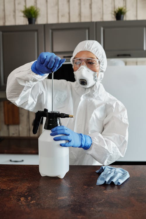 Person in White Protective Suit Holding Black and Blue Plastic Bottle