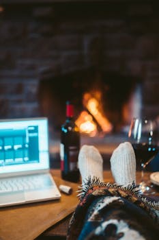 Cozy work-from-home setup with a laptop, red wine, and a warm fireplace ambiance.