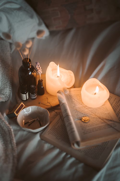 Free Lighted Candle on White Book Beside Black Glass Bottle Stock Photo
