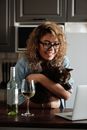 一个女人微笑着抱着猫喝酒，正用笔记本电脑进行视频通话
