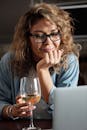 一位女士在家里一边用笔记本电脑，一边喝着白葡萄酒，享受轻松的夜晚