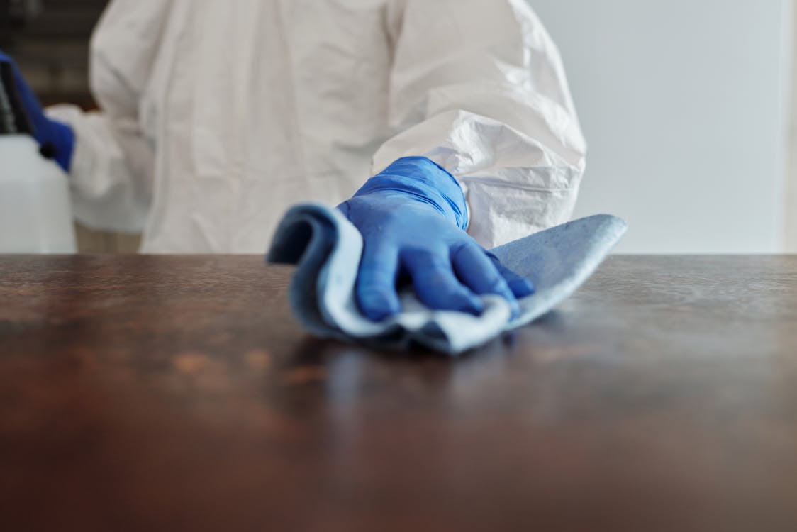 A close-up of a medical facility cleaning services provider with gloves cleaning a desk