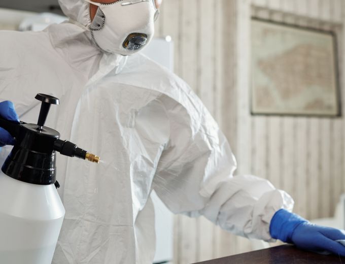 Worker in a protective suit cleaning indoor surfaces