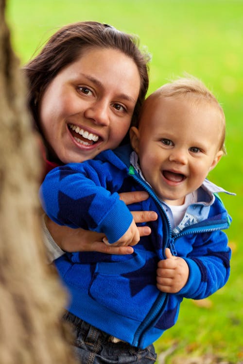 Smiling Woman Carrying Smiling Child Behind Tree Trunk