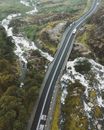 Drone view of vehicles driving along asphalt road running under foaming stream of river and green valley