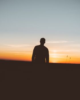 一个男人安详地站在充满活力的日落天空下