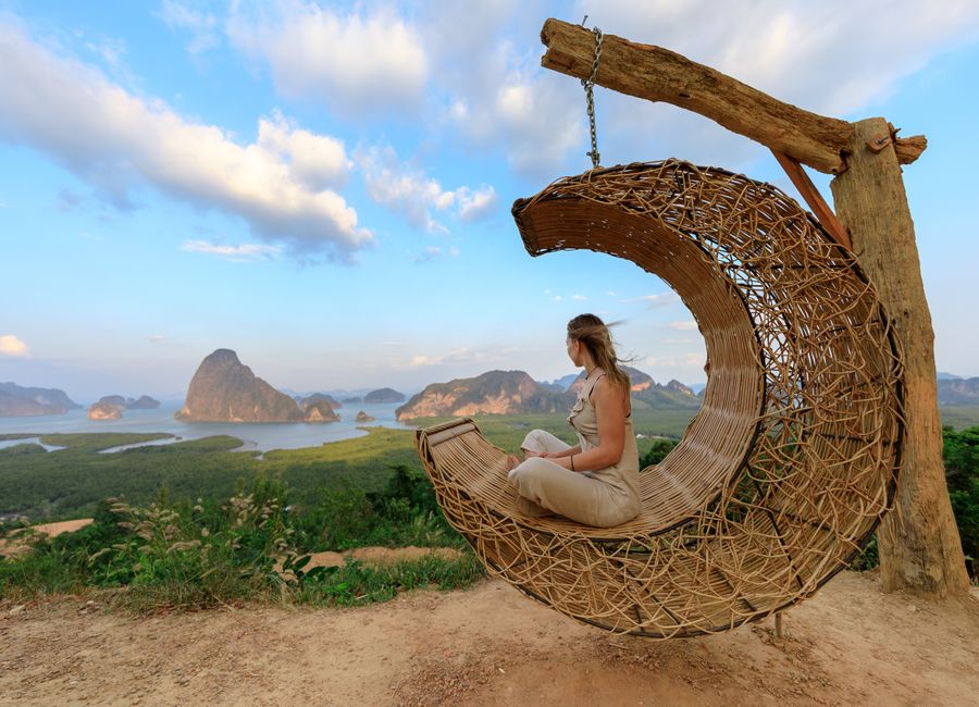 Woman in rattan hammock enjoying Phang-nga Bay's scenic view at sunset.