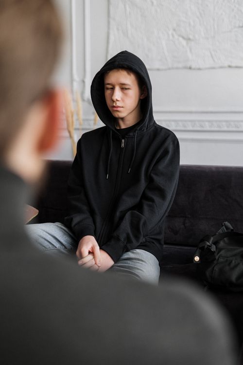 Free A teenager in a black hoodie engages in a counseling session, sitting calmly indoors. Stock Photo