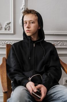 一个穿着黑色连帽衫的青少年坐在室内，神情显得十分沉思
