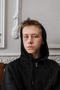 室内一幅十几岁男孩的肖像，他穿着黑色连帽衫，脸上带着轻微瘀伤，神情喜怒无常