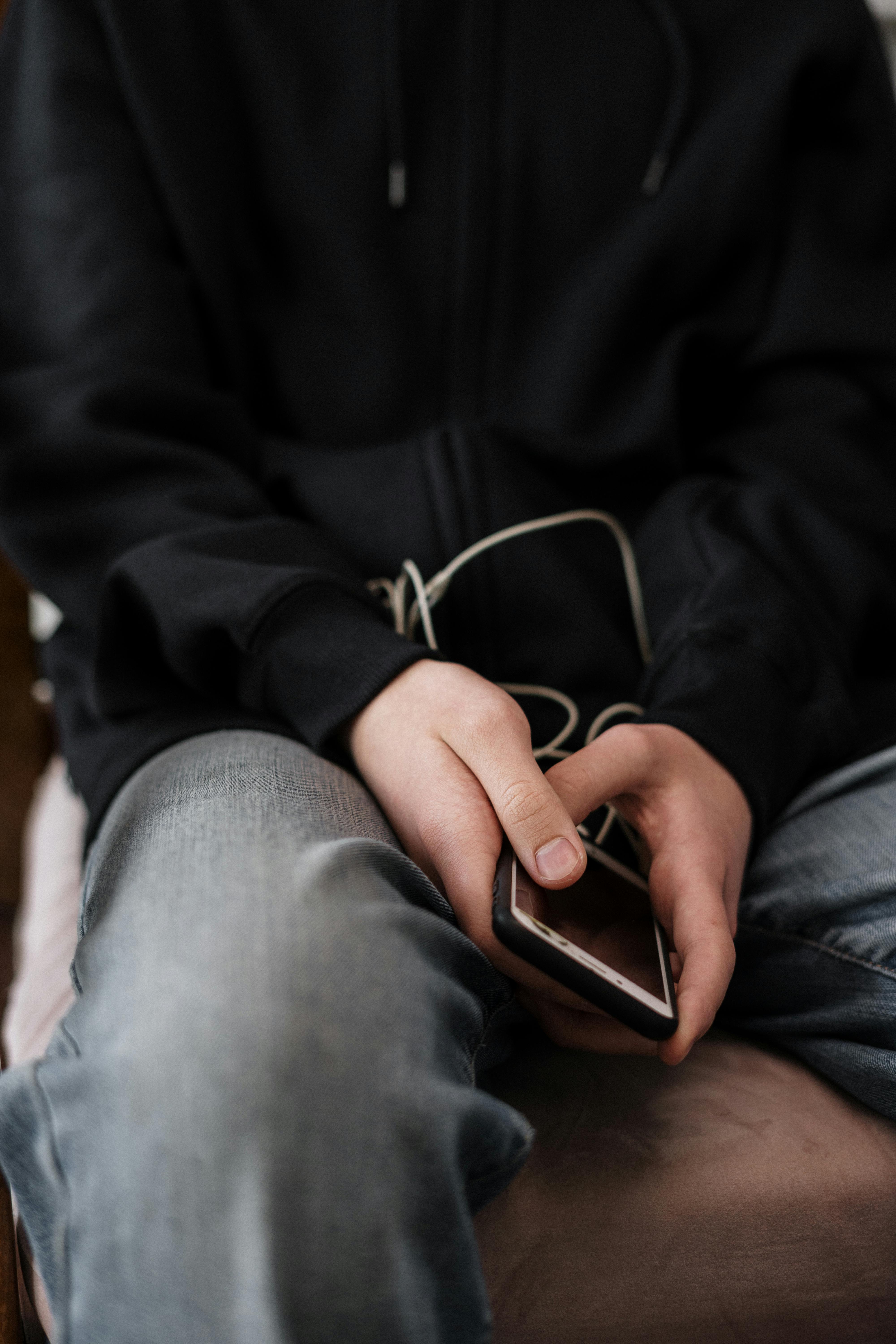 person in black jacket and blue denim jeans holding black smartphone