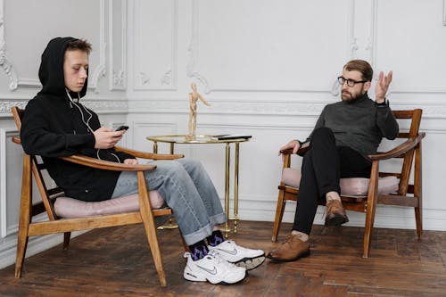 Man in Black Sweater and Blue Denim Jeans Sitting on Brown Wooden Rocking Chair