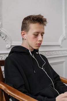 一名穿着黑色连帽衫的青少年戴着耳机坐在室内听音乐