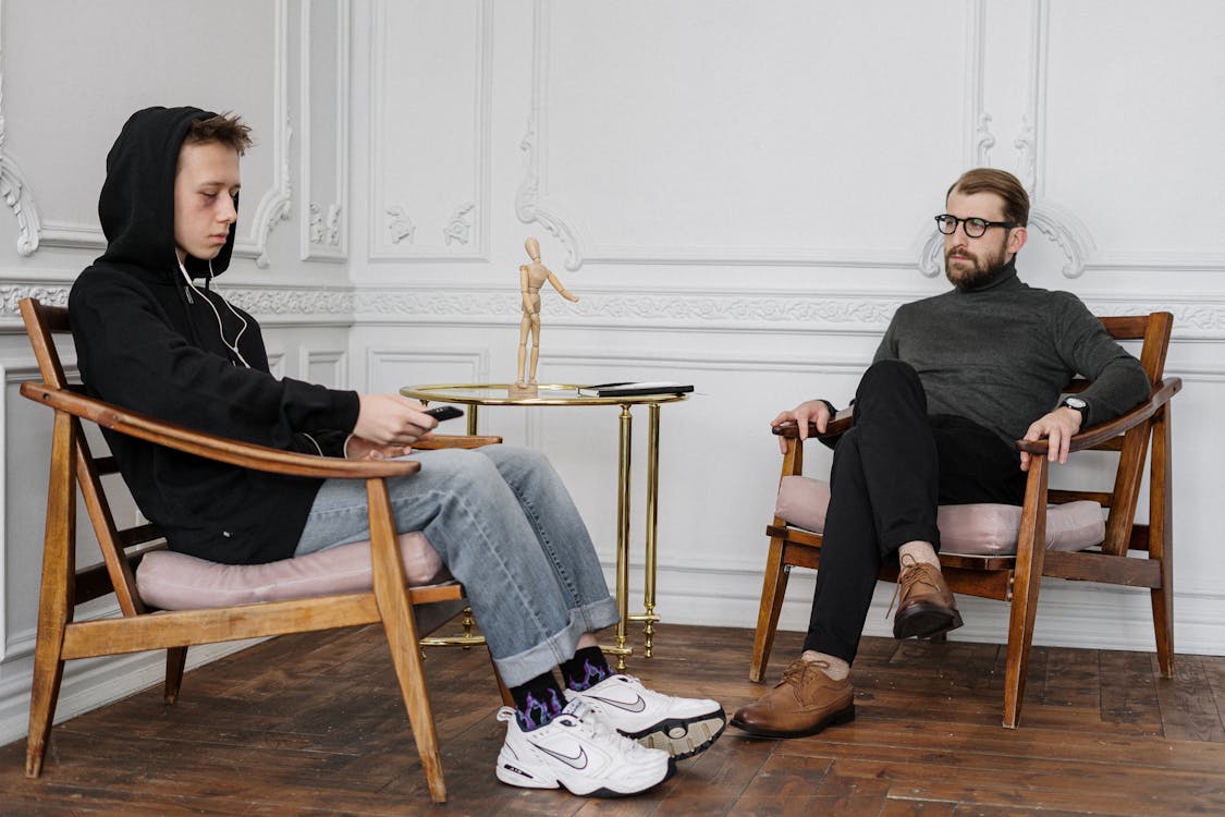 Man in Black Sweater and Blue Denim Jeans Sitting on Brown Wooden Chair