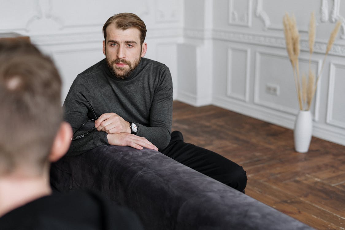 Free Man in Gray Sweater Sitting on Black Couch Stock Photo