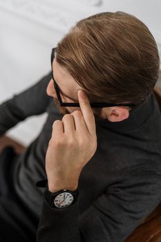 在现代办公室环境中，一名戴眼镜的男子身穿黑色高领毛衣，镜片反射着光线