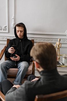 一个十几岁的男孩穿着黑色帽衫，在治疗过程中使用手机