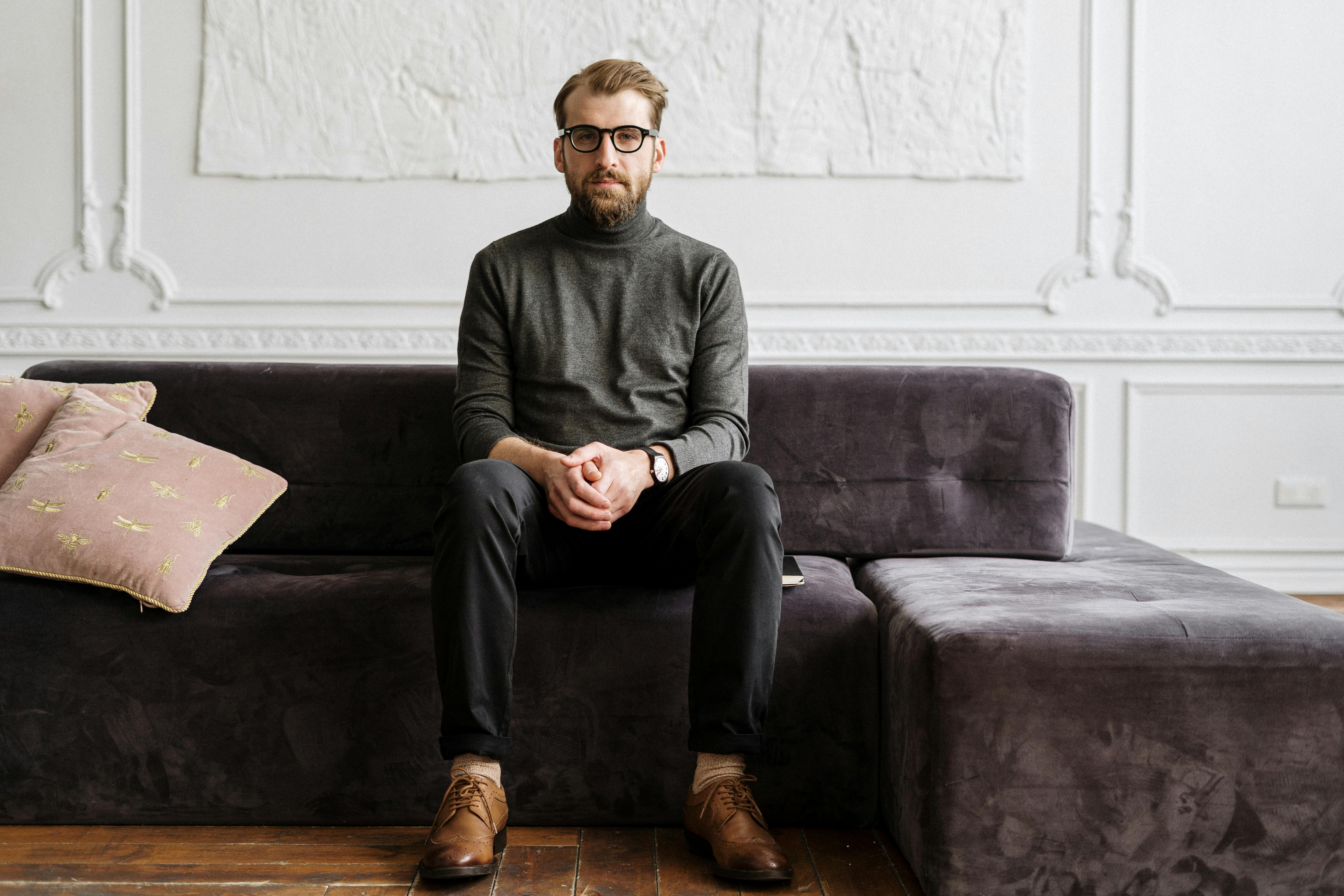 man in black sweater and black pants sitting on gray couch