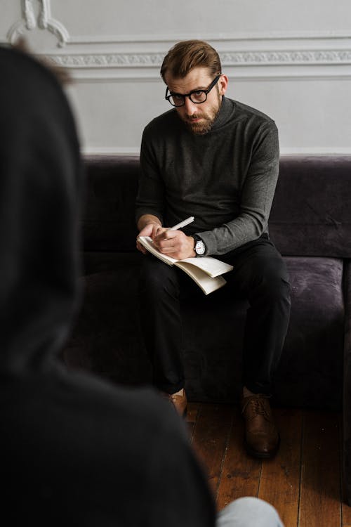 Man in Black Long Sleeve Shirt and Black Pants Sitting on Black Sofa