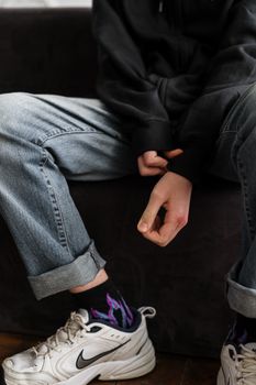 一名穿着连帽衫和牛仔裤的青少年，随意坐在室内，双臂交叉，脚穿白色运动鞋