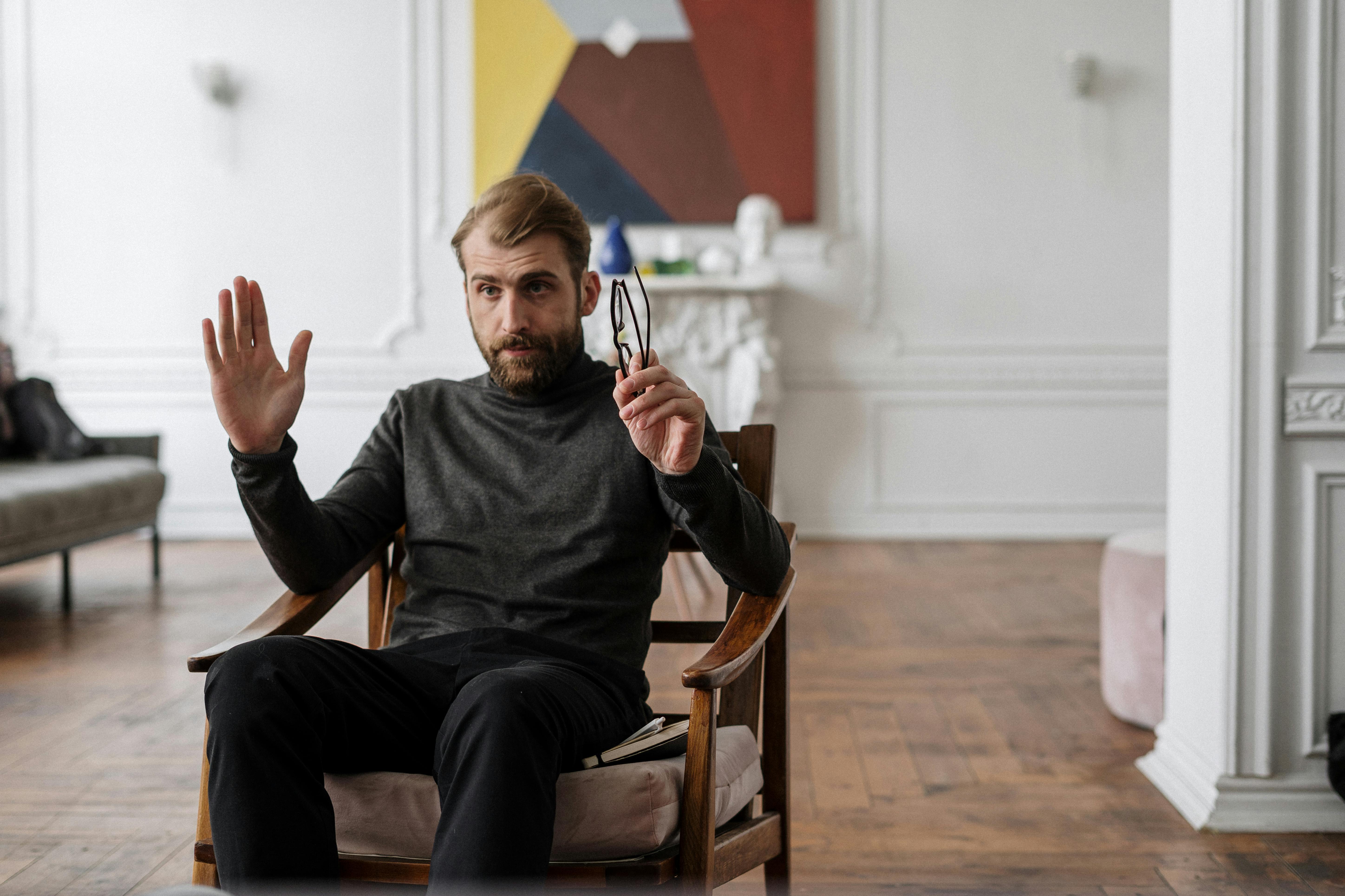 man in black long sleeve shirt sitting on brown wooden armchair