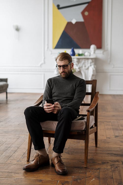 Man in Black Sweater Sitting on Brown Wooden Armchair