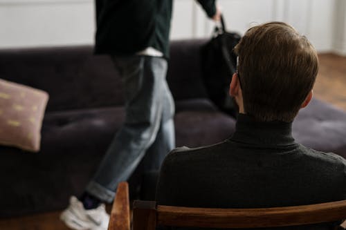 Man in Black Sweater and Blue Denim Jeans Sitting on Brown Wooden Chair