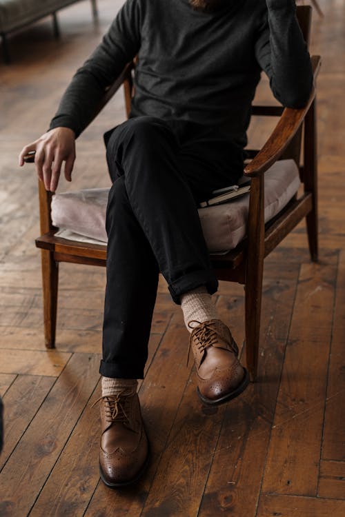 Man in Black Pants and Black Leather Shoes Sitting on Brown Wooden Armchair
