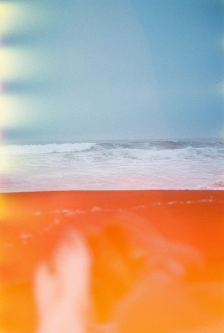 Film photography of a vintage tropical beach scene with orange hues and ocean waves.